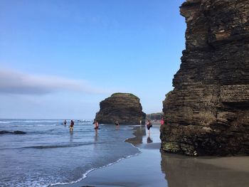 People by rock formation at beach against sky