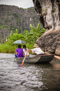 People on rowboat in river against rocky mountains during rainy season
