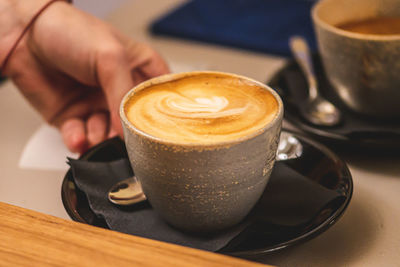 Cup of cappuccino with foam served by the hand of a girl at a bar counter