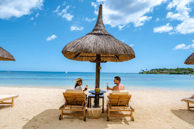 Man and woman sitting at beach against sky