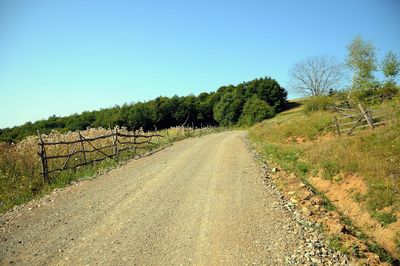 Road amidst trees on field against clear sky