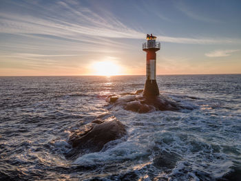 Lighthouse by sea against sky during sunset