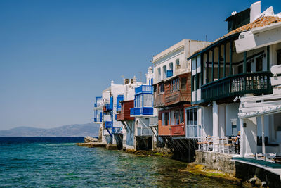 Houses by sea against clear blue sky