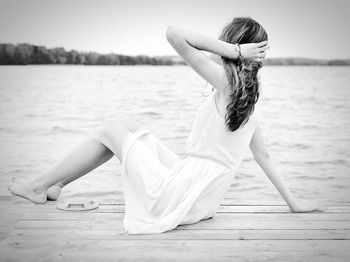 Side view of teenage girl sitting on pier in lake