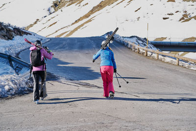 Two skiers carry their skis on their shoulders along the road