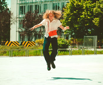 Full length of happy woman jumping on road in city