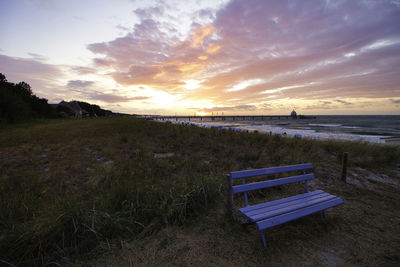 Empty bench by sea against sky during sunset