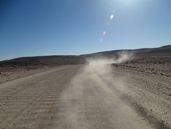 Dirt road amidst land against clear sky