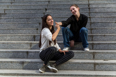 Female friends gesturing thumbs up while sitting on steps