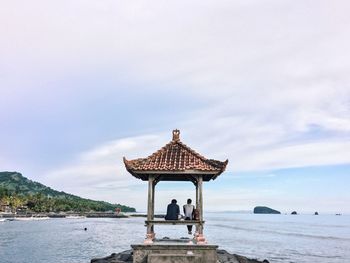 Rear view of men sitting at gazebo in sea against sky