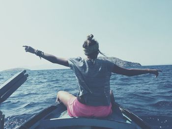 Rear view of woman with arms outstretched on boat sailing in sea