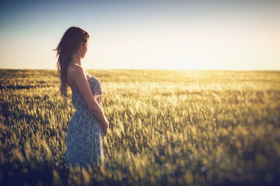 Side view of woman standing on grassy field against clear sky