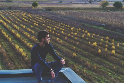 Man sitting on building terrace against farm