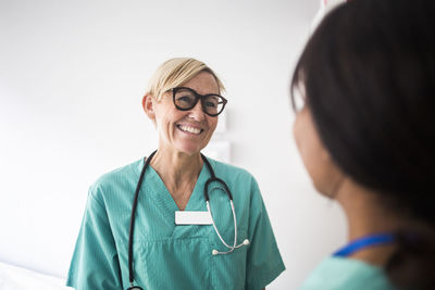 Smiling mature pediatrician talking to female coworker while standing in clinic