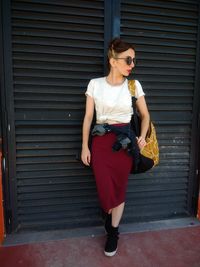 Full length of fashionable woman standing against closed shutter