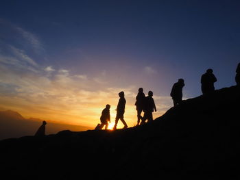 Silhouette people on shore against sky during sunset