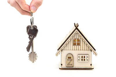 Cropped hand of woman holding key over model home with paper currencies against white background