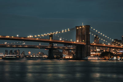 Illuminated bridge over river against sky in city at night