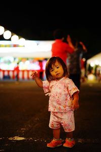 Portrait of cute baby girl standing on road against sky at night