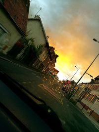 Cars parked on street against cloudy sky at sunset