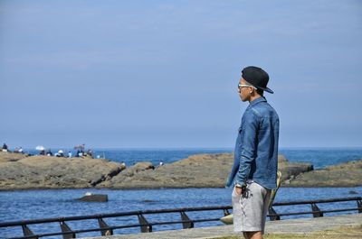 Young man standing on pier over sea against sky