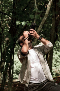 Side view of young man photographing while standing in forest