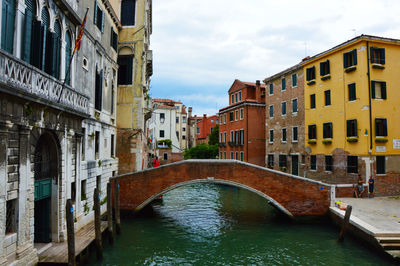 Footbridge over canal in city against sky