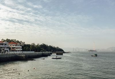 Boats sailing in river against cloudy sky