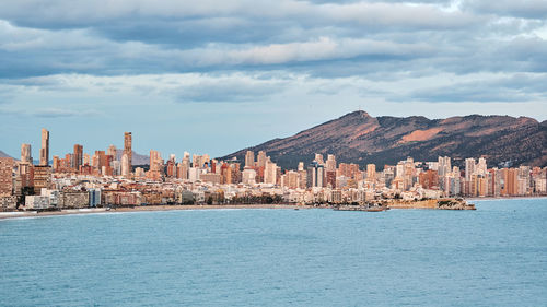 View of buildings by sea against cloudy sky