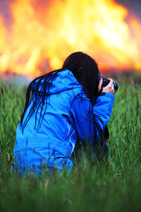 Rear view of woman photographing fire on grassy field