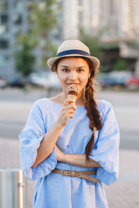 Portrait of young woman eating ice cream in city