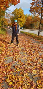 Full length of woman standing amidst leaves during autumn