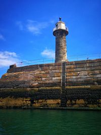 Lighthouse by building against sky