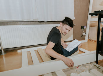 A young man collects bolts according to the instructions for assembling a bed.