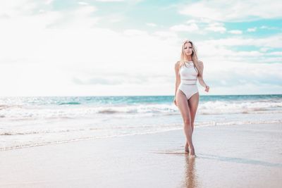 Full length of woman in swimwear walking on beach against sky