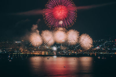 Firework display over illuminated city against sky at night