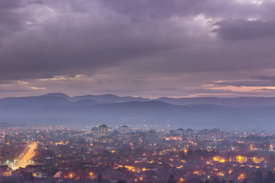 Illuminated buildings in city against sky at sunset