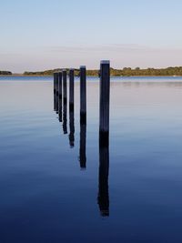 Wooden posts in lake against sky