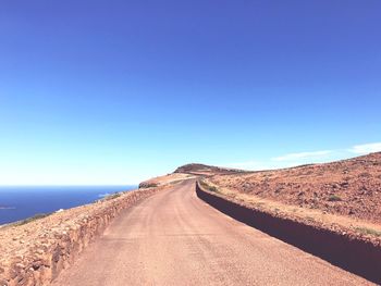 Road amidst land against clear blue sky