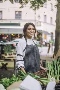 Portrait of smiling female vendor selling vegetables at organic market