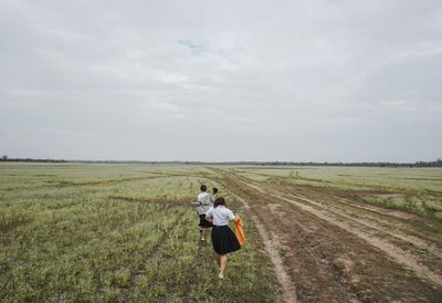 Rear view of man and woman walking on field