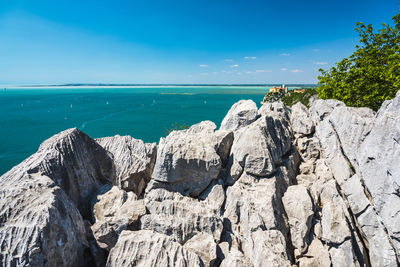 Scenic view of rocks by sea against blue sky