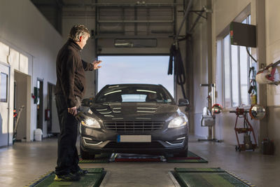 Full length of mechanic showing stop gesture towards car on hydraulic lift