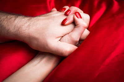 Cropped image of couple holding hands on bed