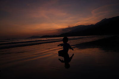 Silhouette man standing on beach against sky during sunset