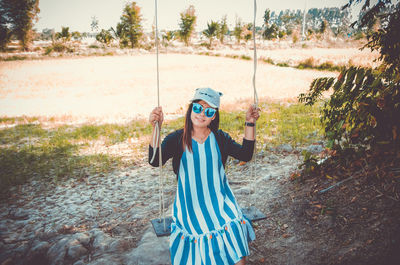 Portrait of smiling young woman sitting on swing on land