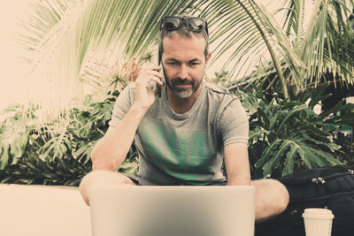 Man using mobile phone and laptop while sitting on seat by plants