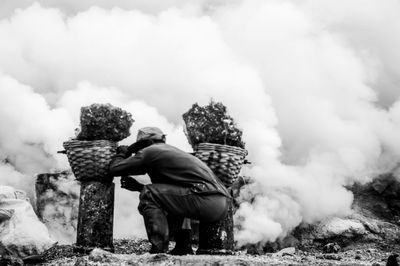 Rear view of woman sitting on rock against sky