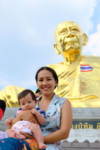 Portrait of mother and daughter in front of budhist temple and the thai flag