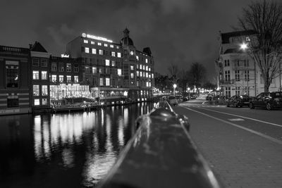 Illuminated street by buildings against sky at night